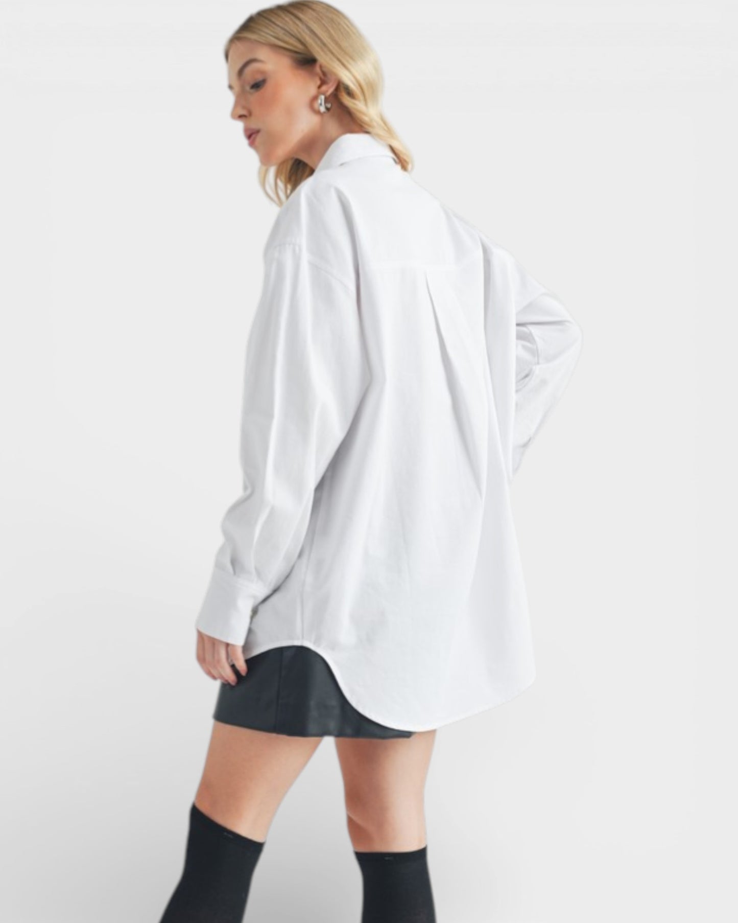 Person wearing a white oversized shirt and black shorts on a plain background