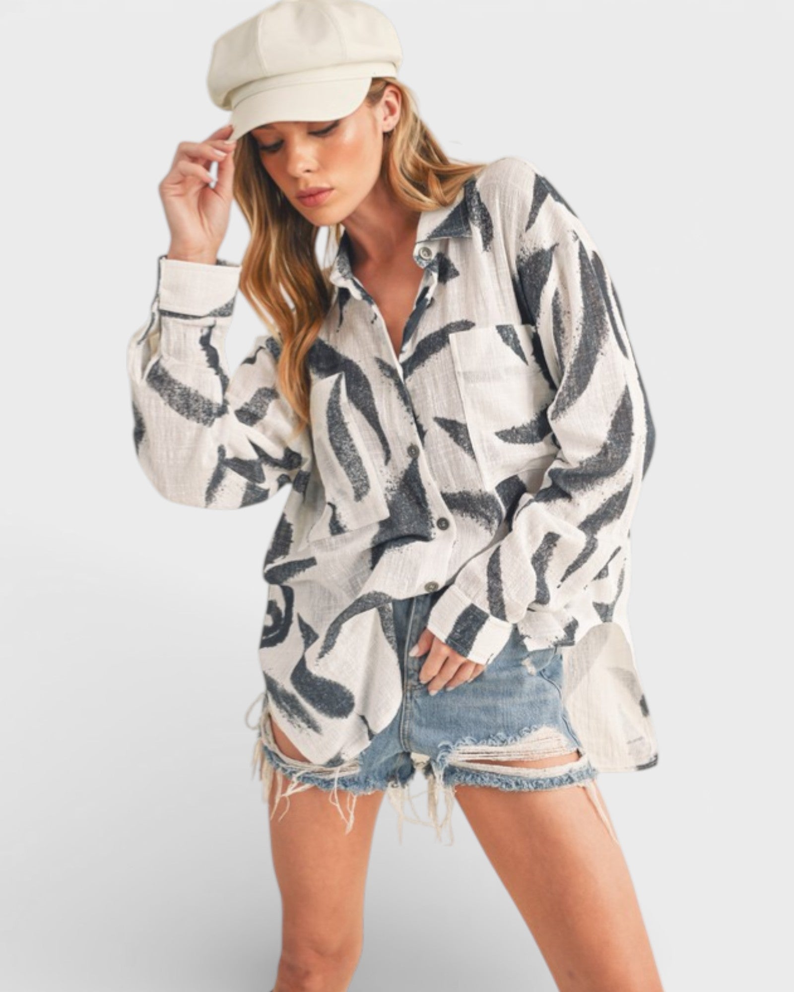 Woman wearing a patterned shirt, denim shorts, and a cap on a white background