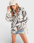 Woman wearing a patterned shirt, denim shorts, and a cap on a white background