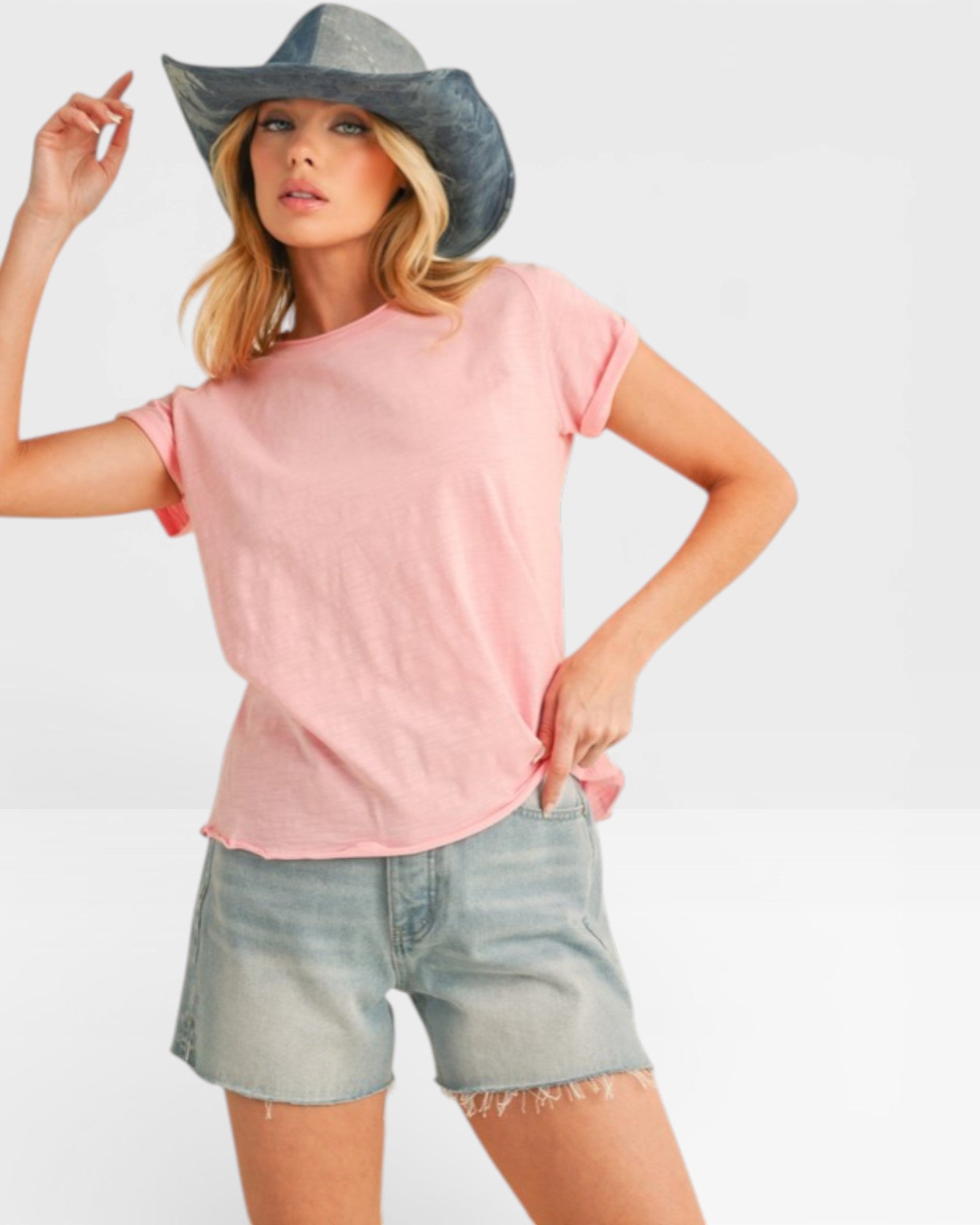 Woman wearing a pink t-shirt and denim shorts with a gray hat on a white background