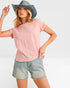 Woman wearing a pink t-shirt and denim shorts with a gray hat on a white background