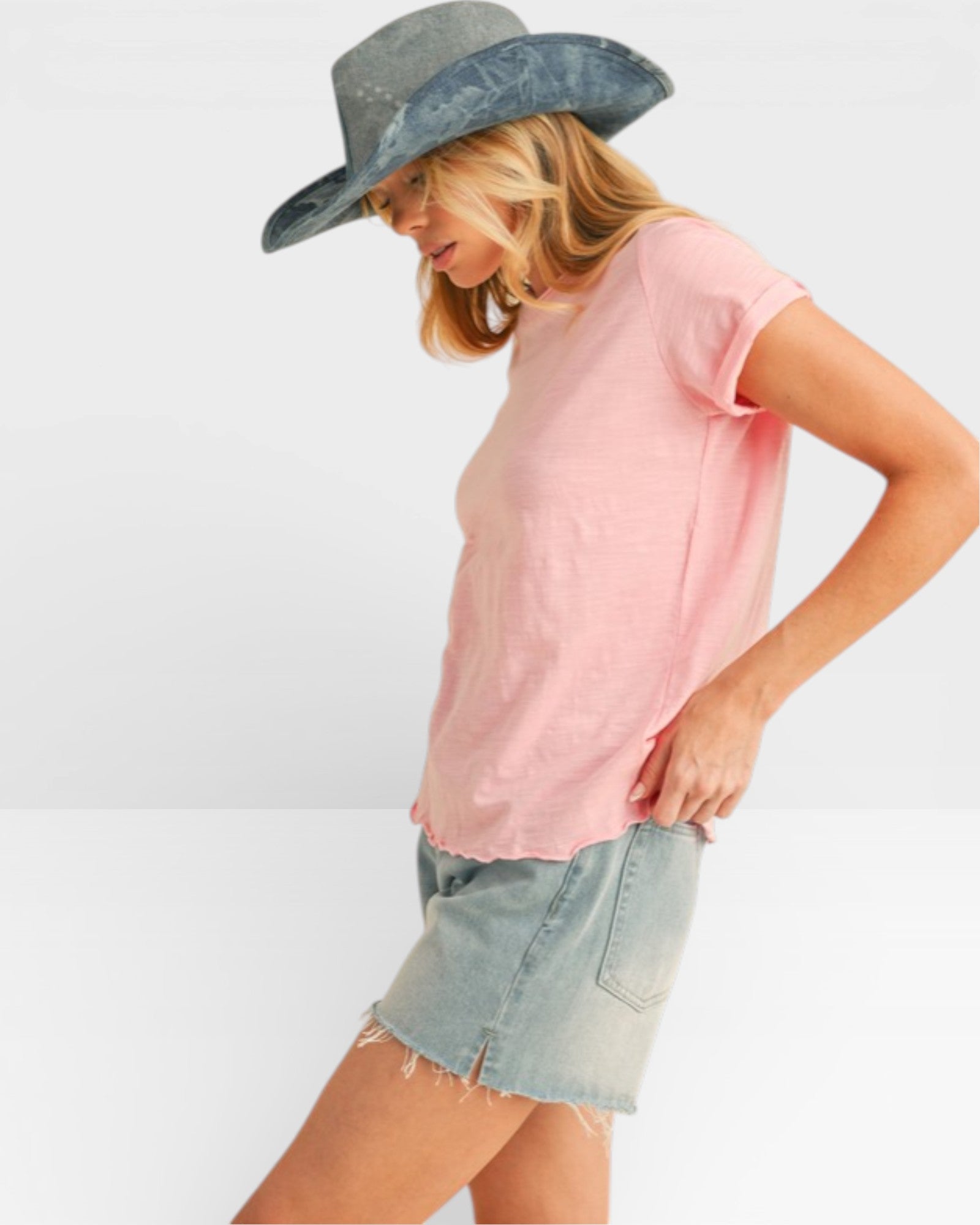 Woman wearing a pink t-shirt, denim shorts, and a wide-brimmed hat on a white background