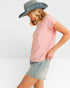 Woman wearing a pink t-shirt, denim shorts, and a wide-brimmed hat on a white background