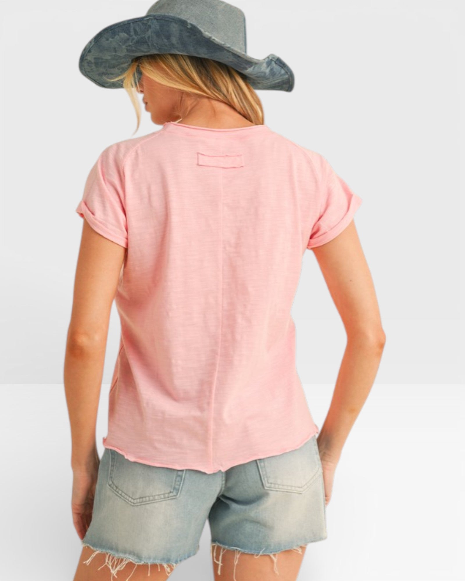 Person wearing a pink t-shirt and denim shorts with a wide-brimmed hat on a white background