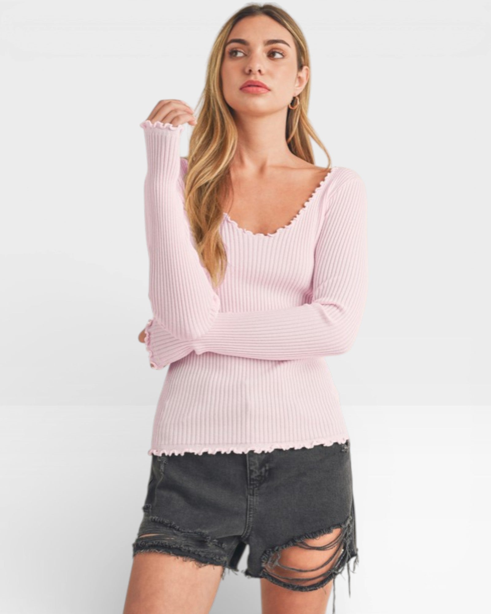 Woman wearing a light pink sweater and black shorts on a white background