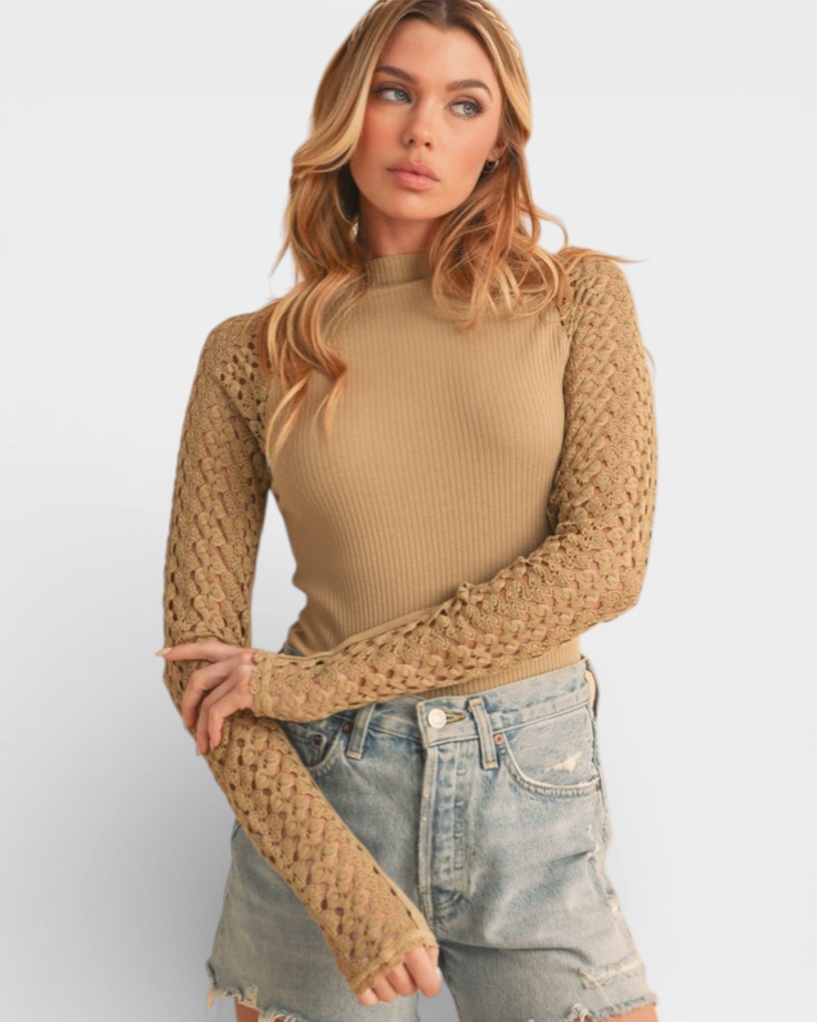 Woman wearing a beige ribbed sweater with mesh sleeves on a plain background