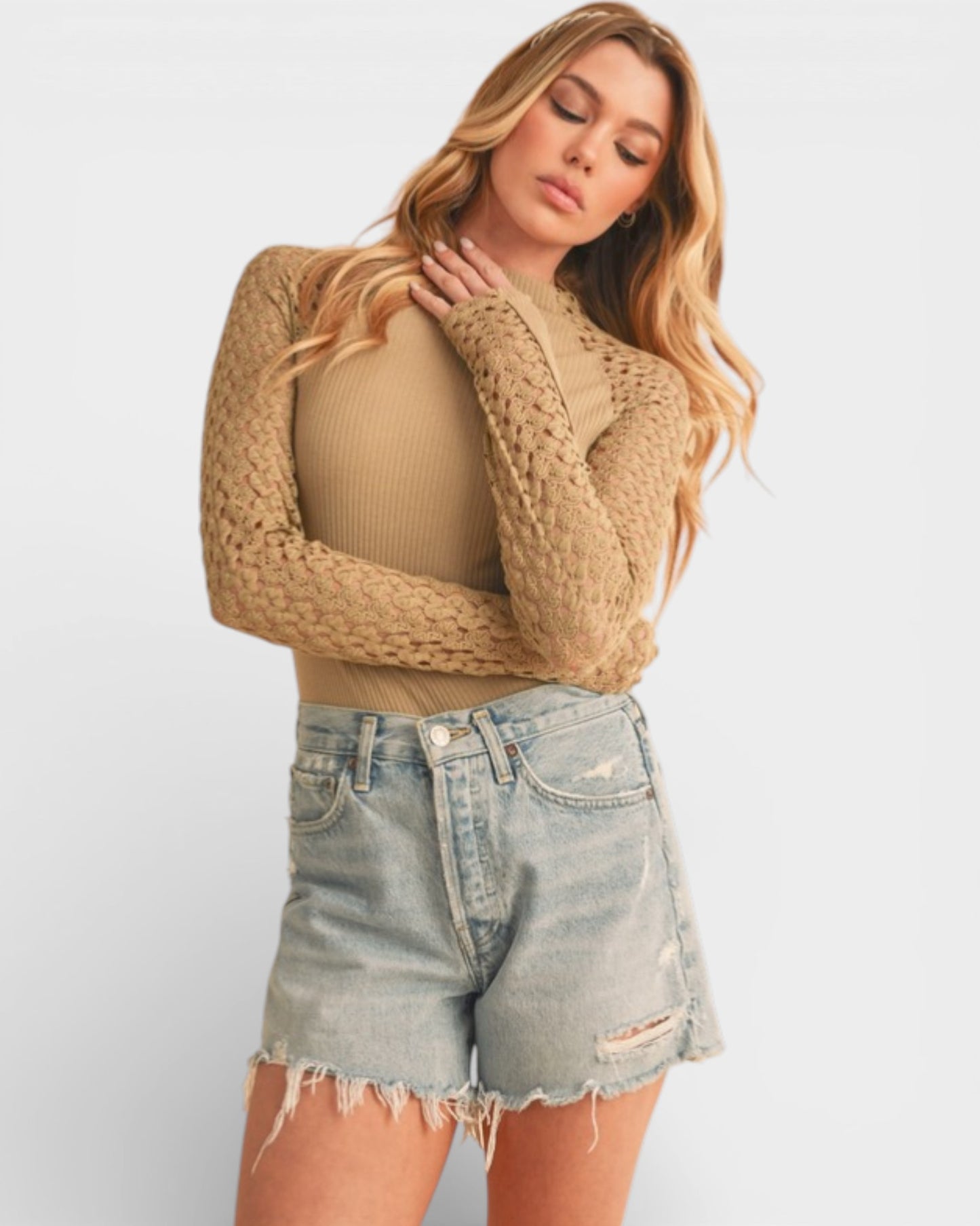 Woman wearing a beige ribbed top and denim shorts on a plain background