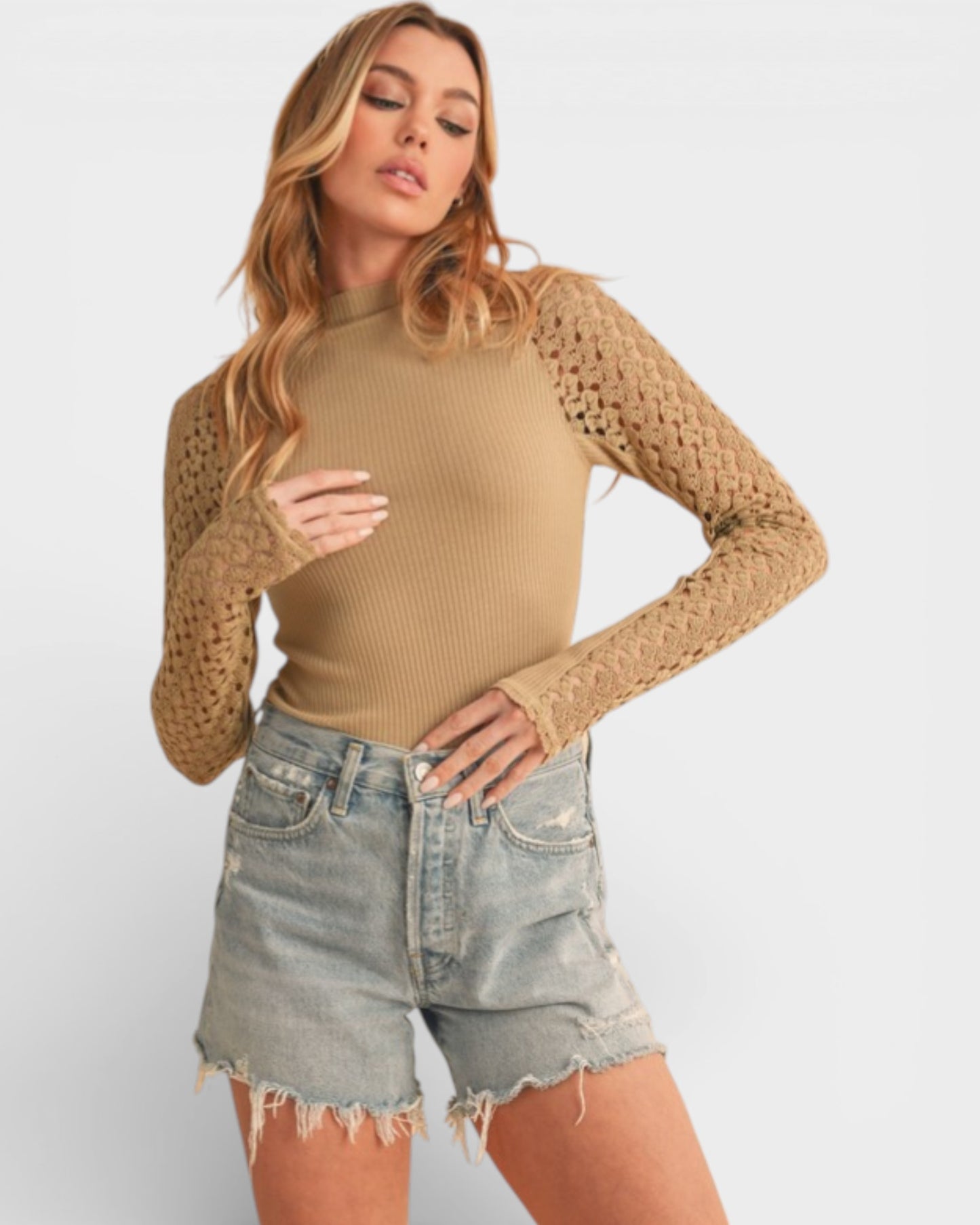 Woman wearing a beige mesh top and denim shorts on a white background