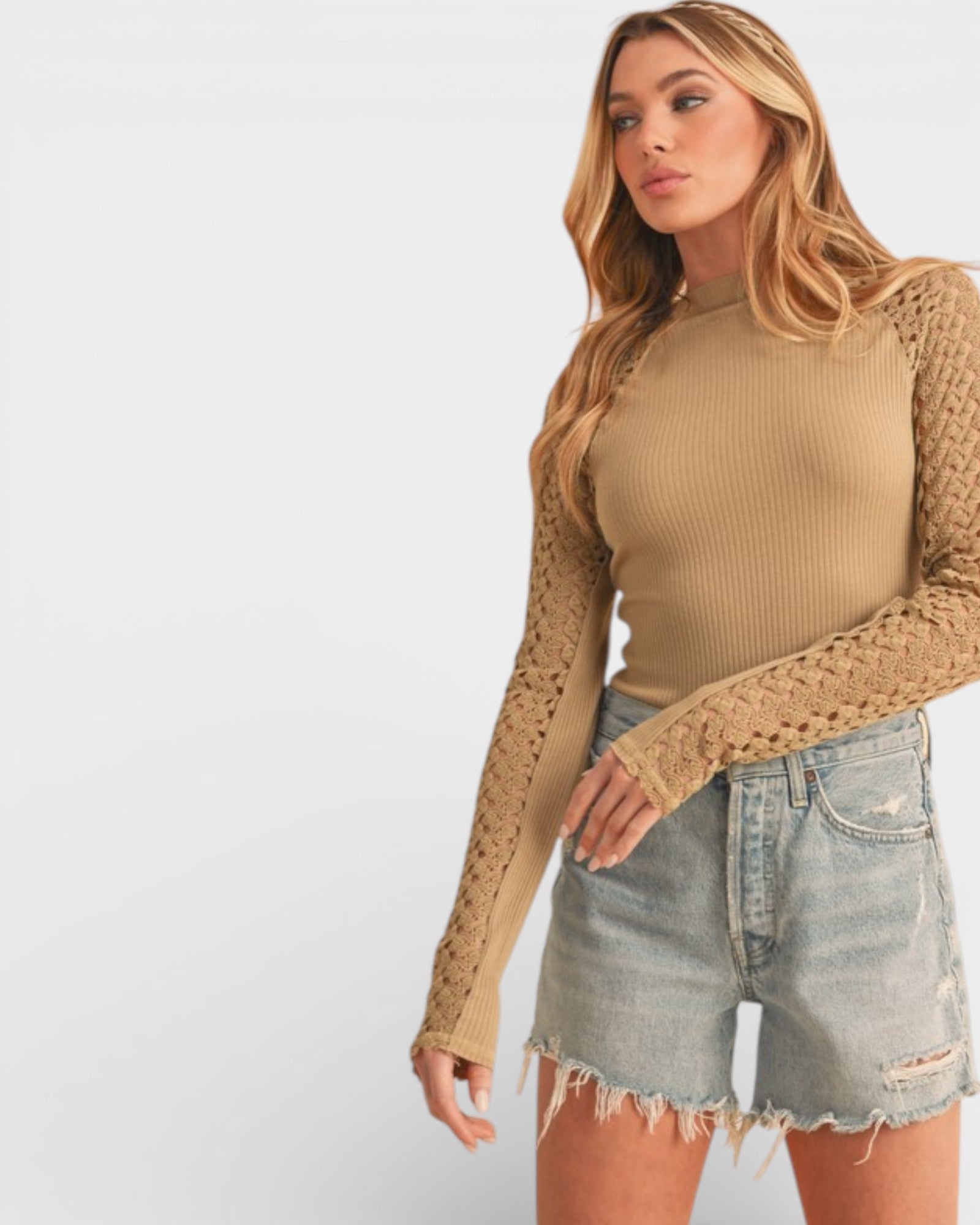 Woman wearing a beige ribbed top with lace sleeves and denim shorts on a white background
