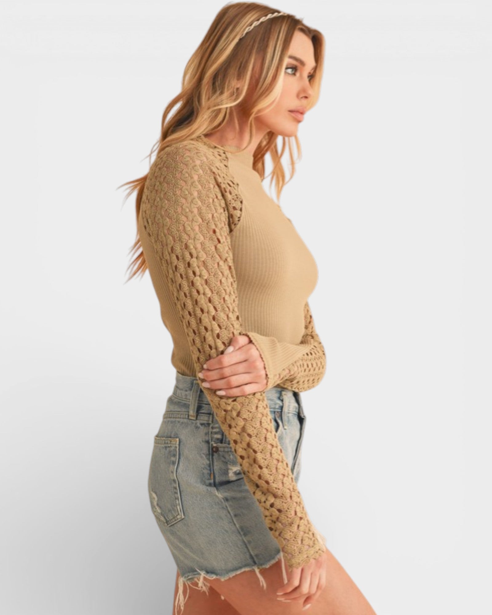 Woman wearing a beige knitted sweater and denim shorts on a white background