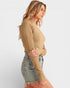 Woman wearing a beige knitted sweater and denim shorts on a white background