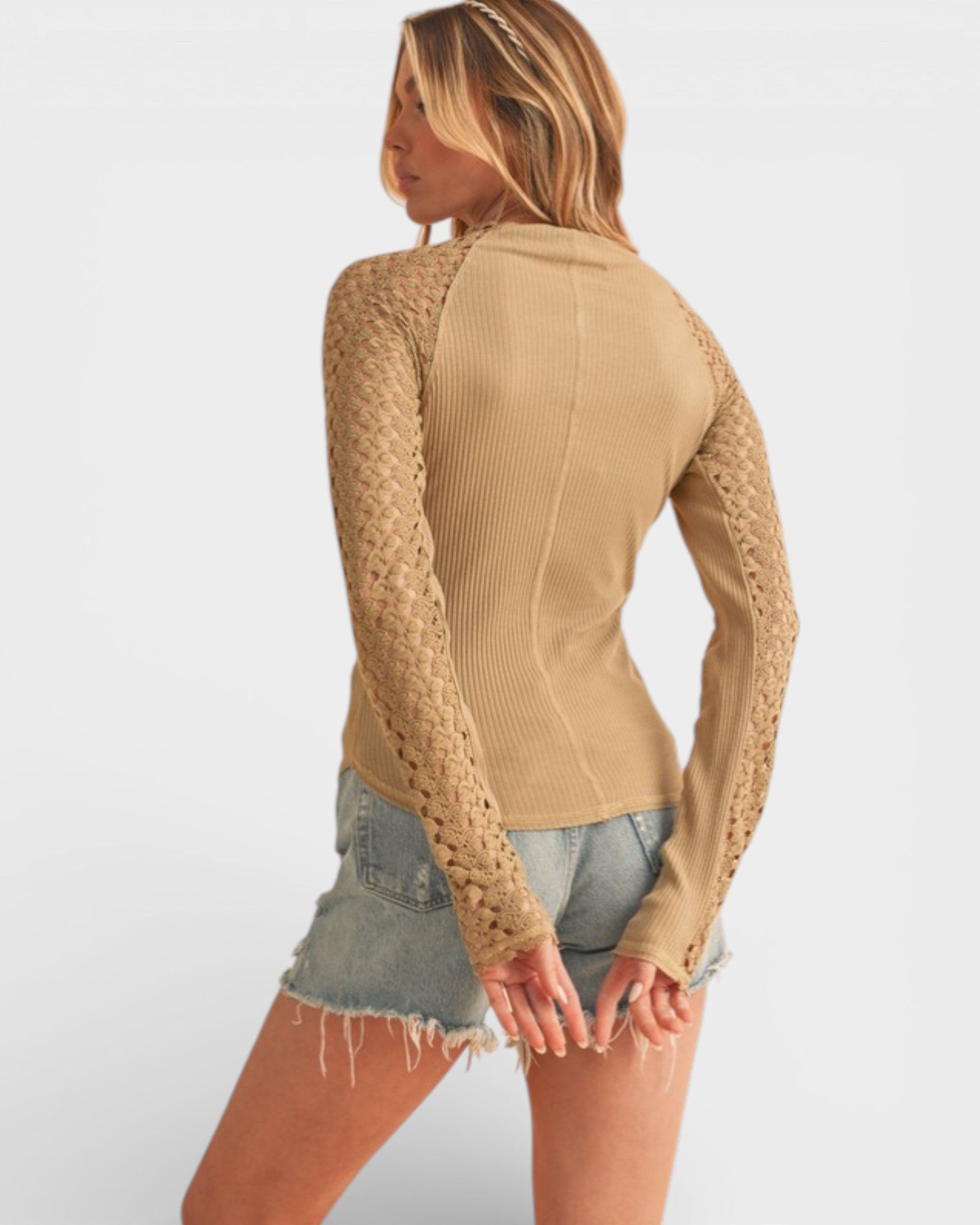 Woman wearing a beige ribbed sweater and denim shorts on a white background