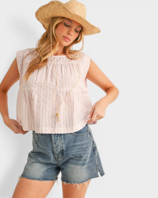 Woman wearing a light pink top and denim shorts with a straw hat on a white background