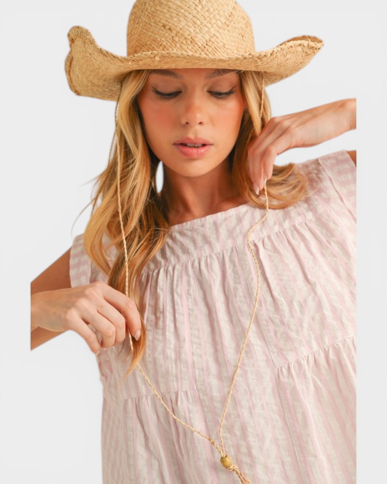 Woman wearing a straw hat and light pink dress with a long necklace.