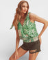 Woman wearing a green patterned top and black shorts on a white background