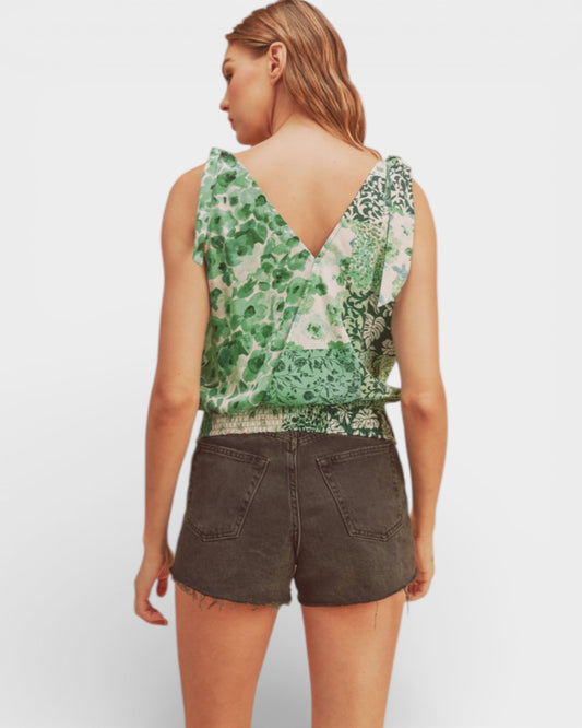 Woman wearing a green patterned sleeveless top and dark shorts on a white background