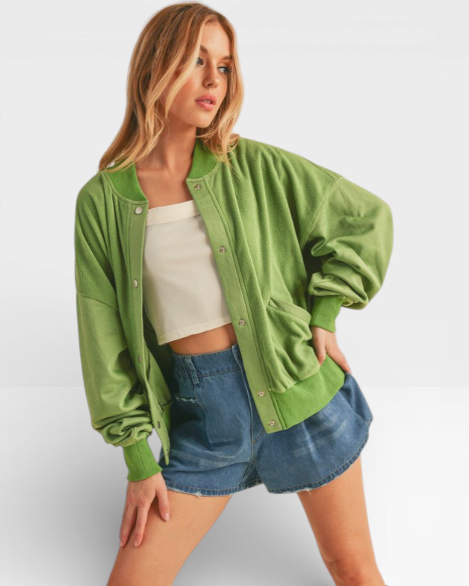 Woman wearing a green jacket, white top, and denim shorts on a light gray background