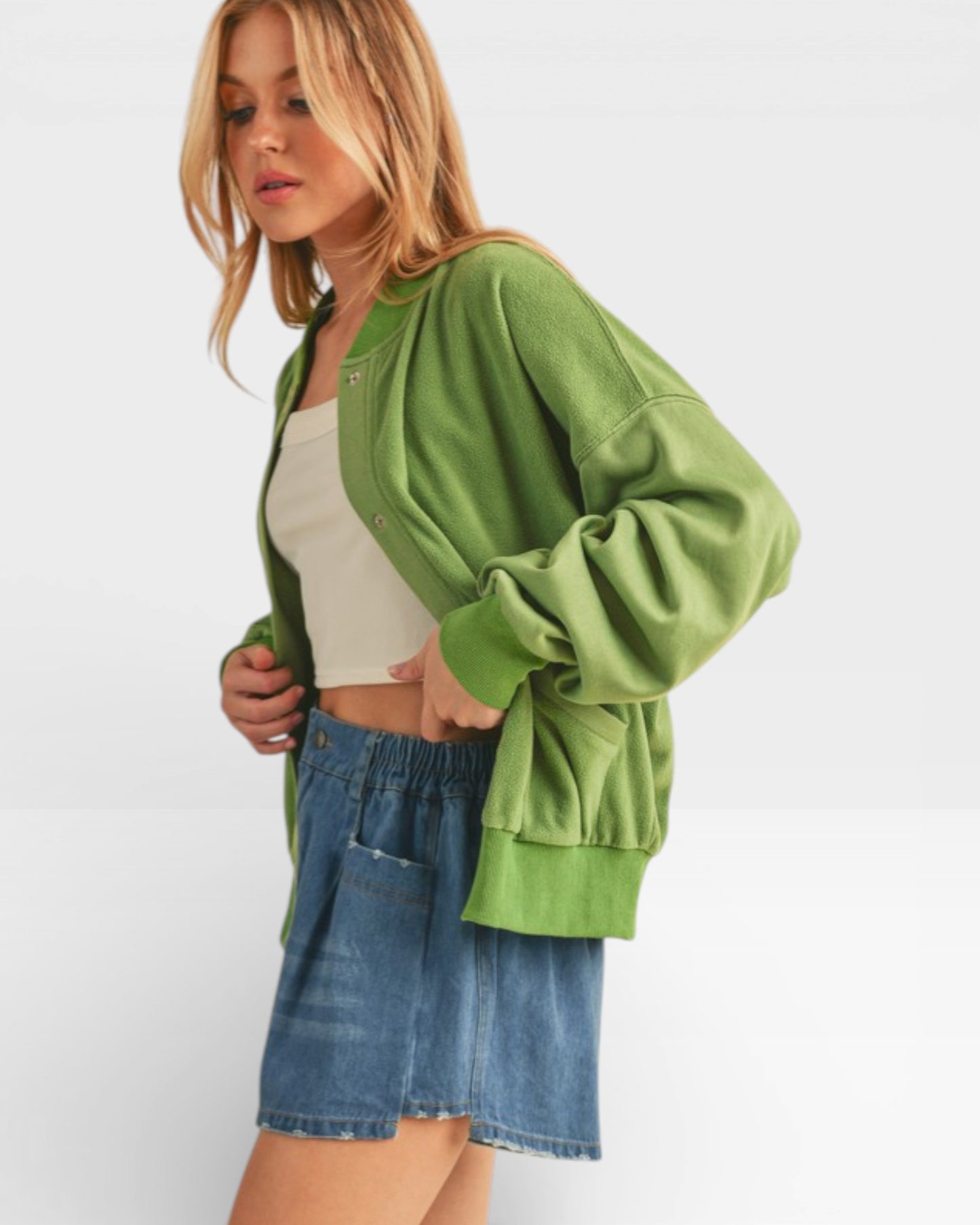Woman wearing a green jacket, white top, and denim shorts on a white background