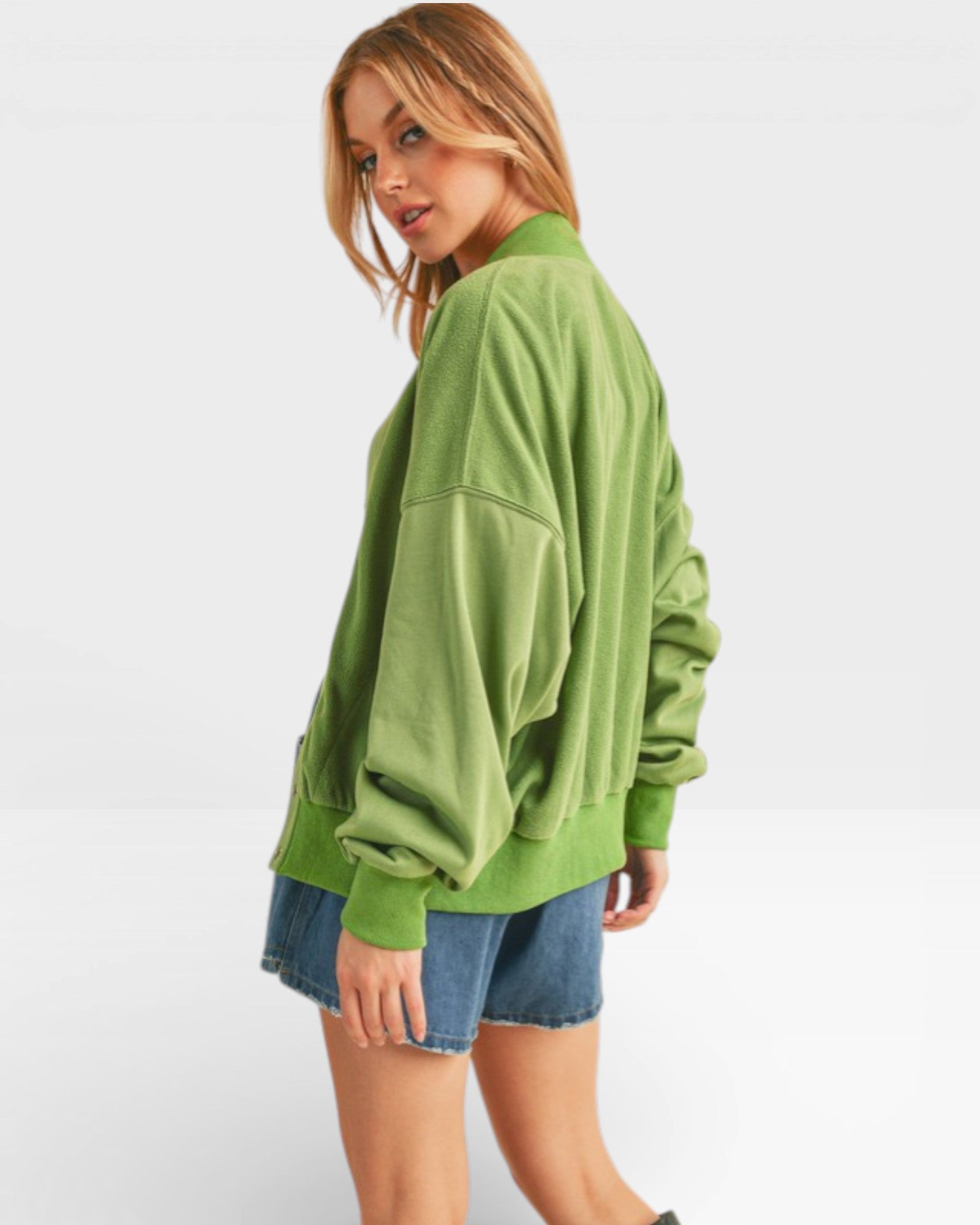 Woman wearing a green oversized sweater and denim shorts on a white background