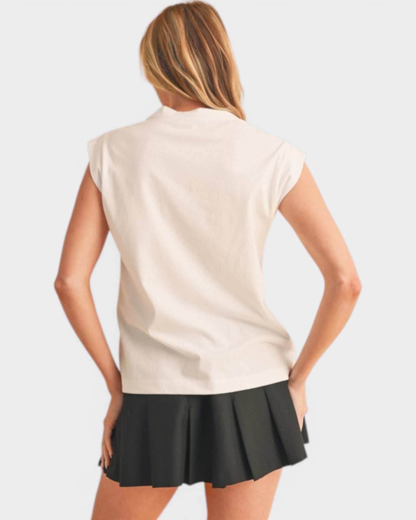 Woman wearing a beige sleeveless top and black skirt on a plain background