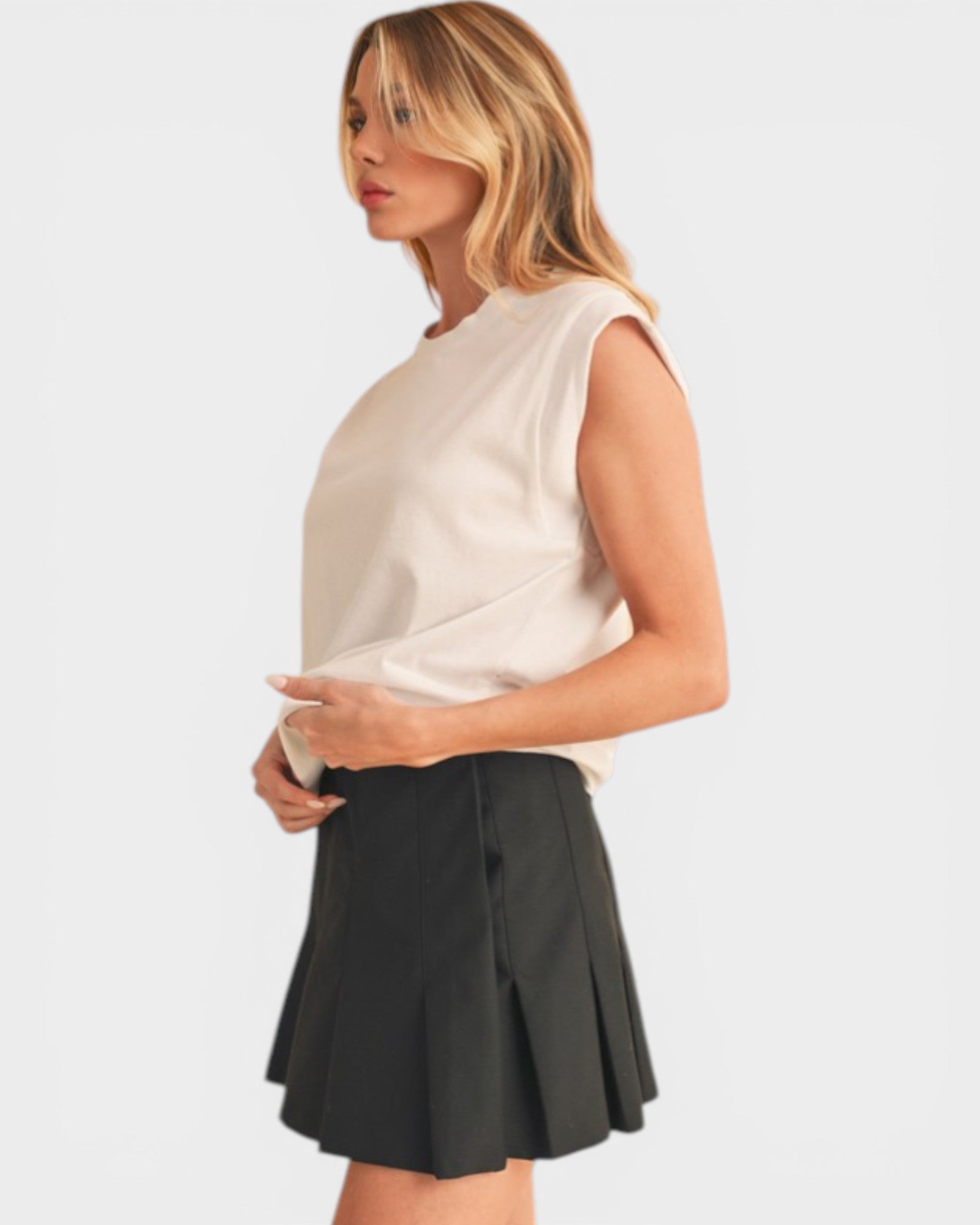 Woman wearing a white sleeveless top and black skirt on a light gray background