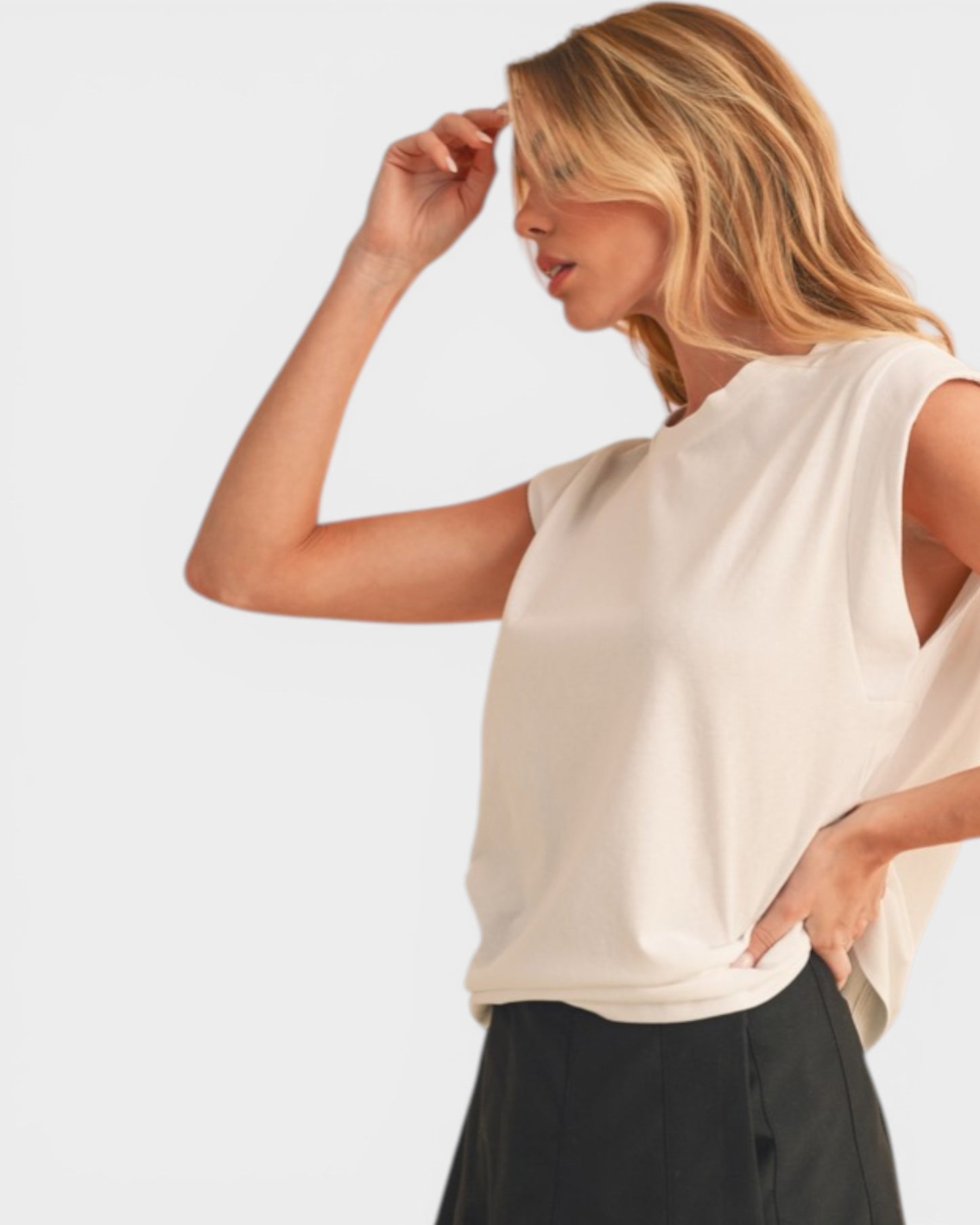 Woman wearing a beige sleeveless top and black pants on a light gray background