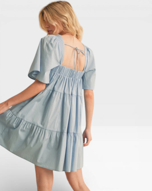 Woman wearing a light blue dress with a tiered skirt and open back on a plain background