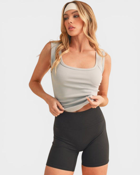 Woman wearing a light gray tank top and black shorts on a white background