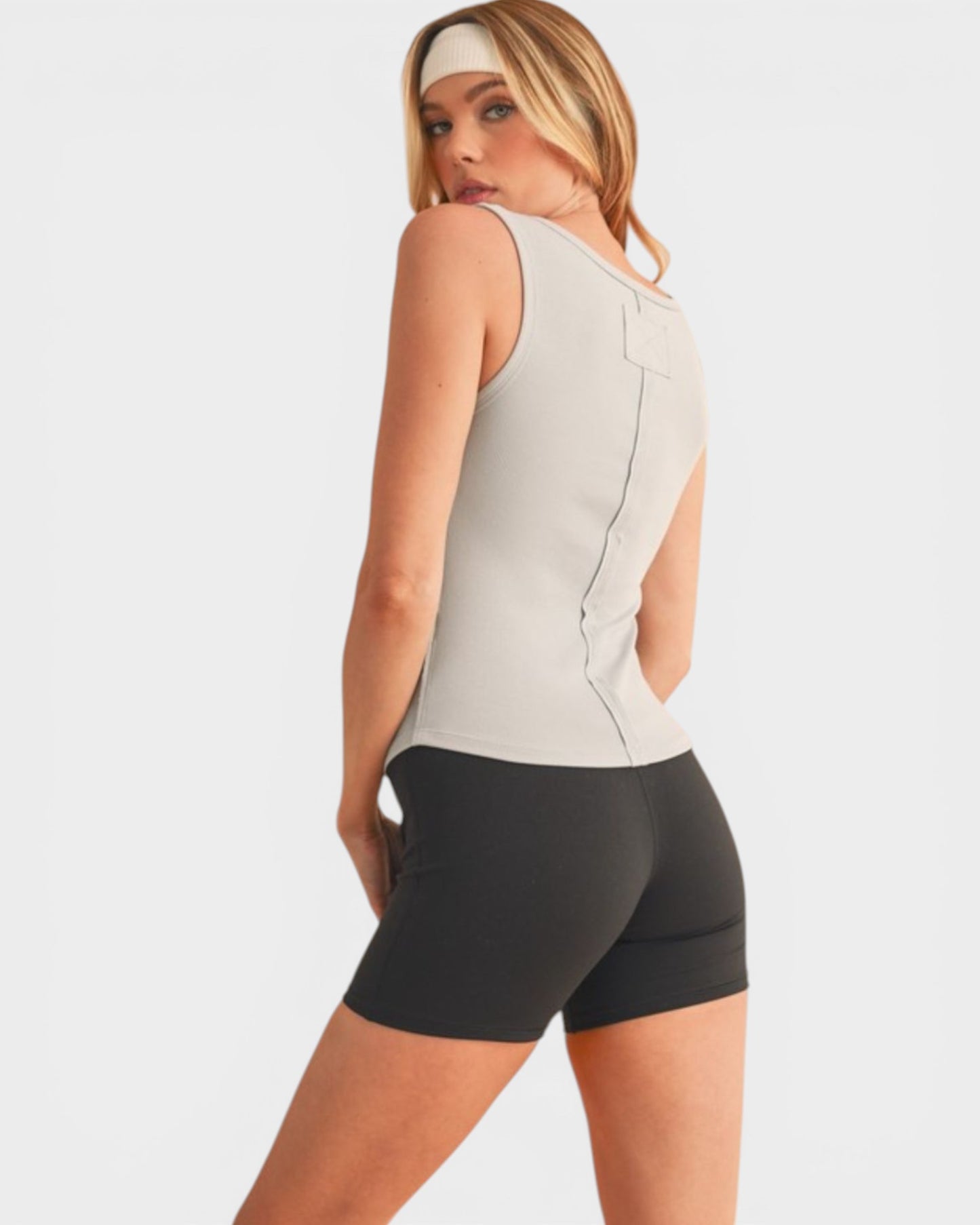Woman wearing a beige sleeveless top and black shorts on a white background