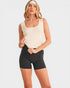 Woman wearing a beige tank top and black shorts on a white background