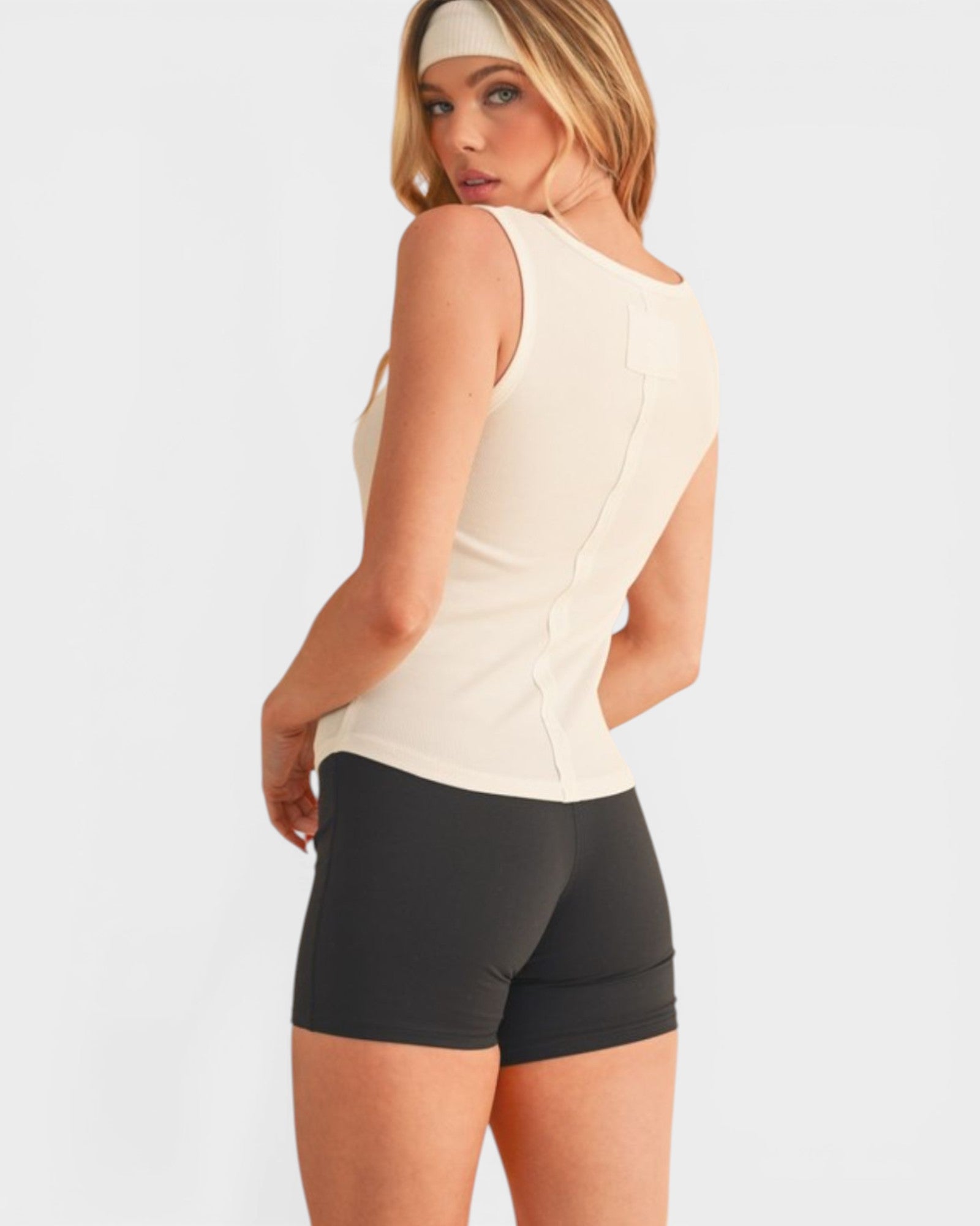 Woman wearing a beige sleeveless top and black shorts on a white background