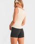 Woman wearing a beige sleeveless top and black shorts on a white background