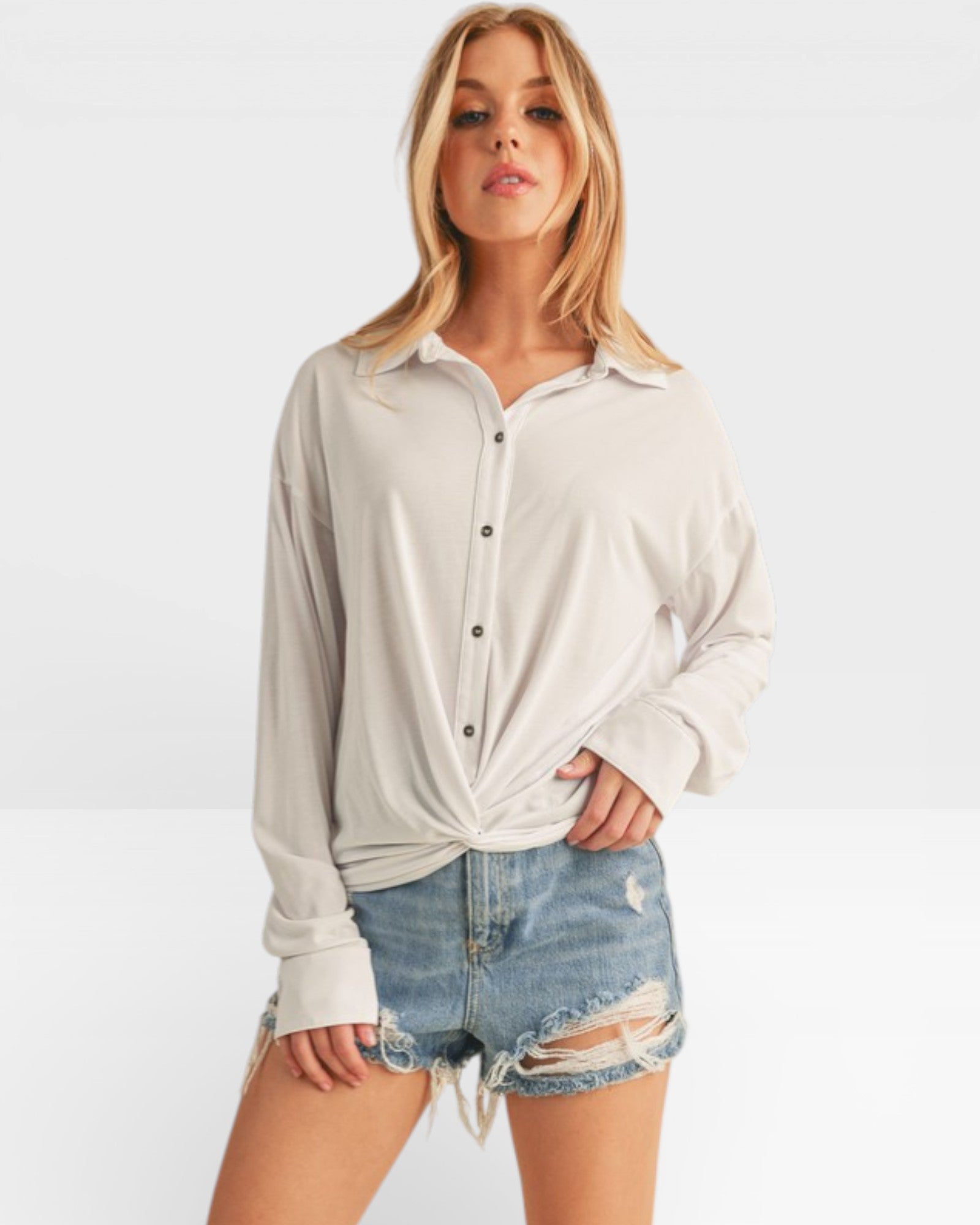 Woman wearing a light gray button-up shirt and denim shorts on a white background