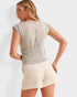 Woman wearing a beige top and cream shorts on a white background