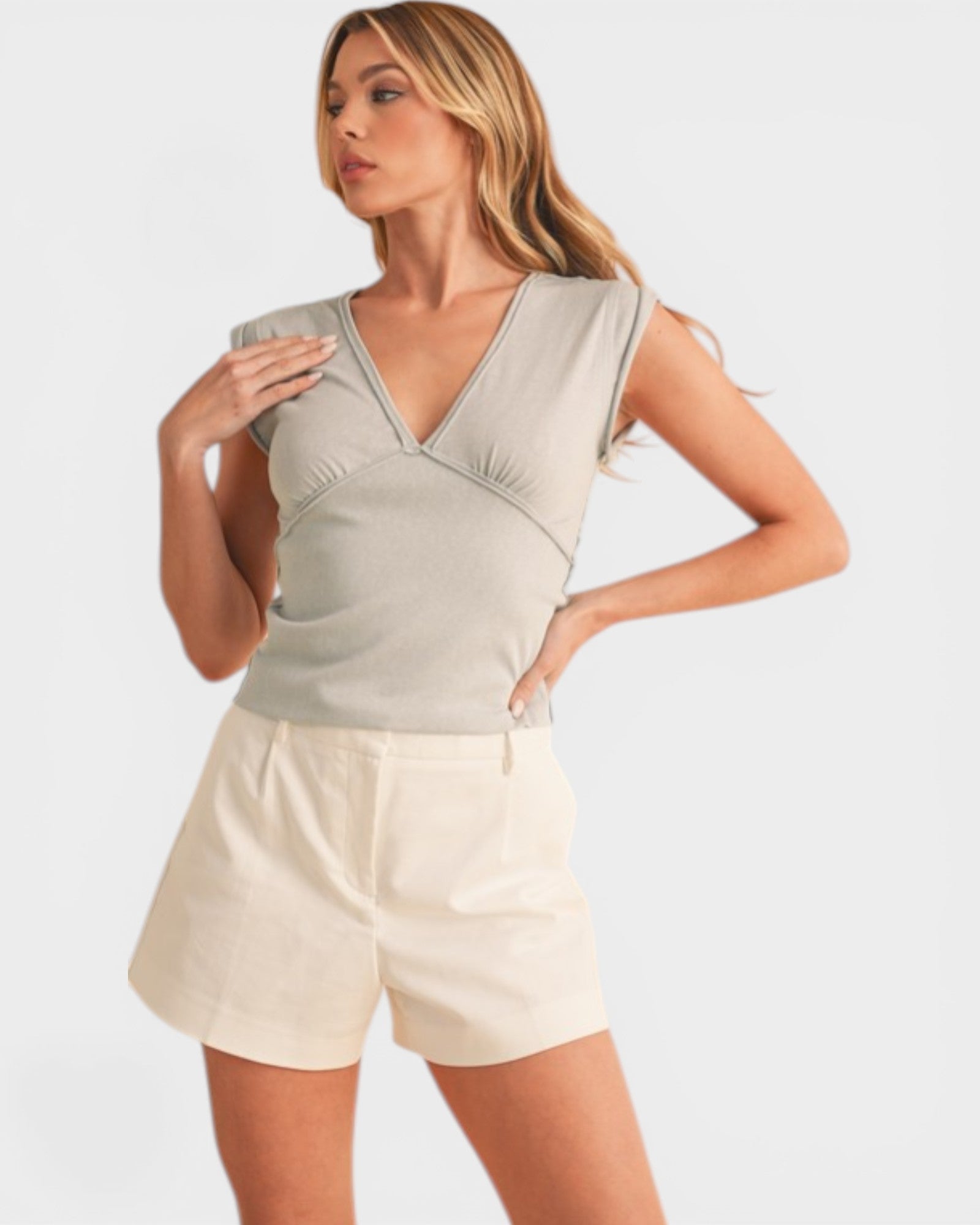 Woman wearing a light gray top and white shorts on a plain background