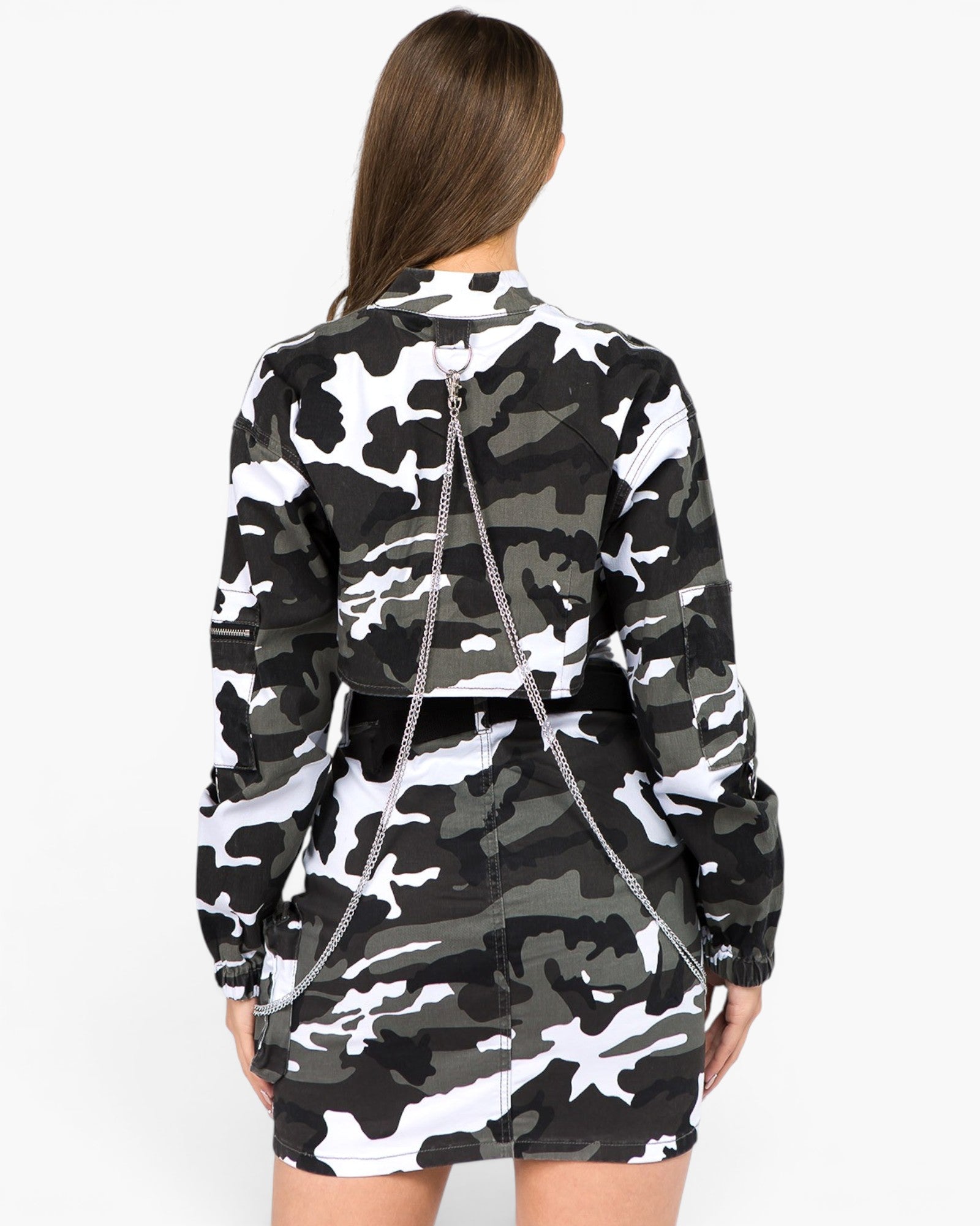 A model shown from the back wearing a black, white, and gray camouflage long-sleeve mini dress with a silver chain detail running down the back, set against a plain white background.