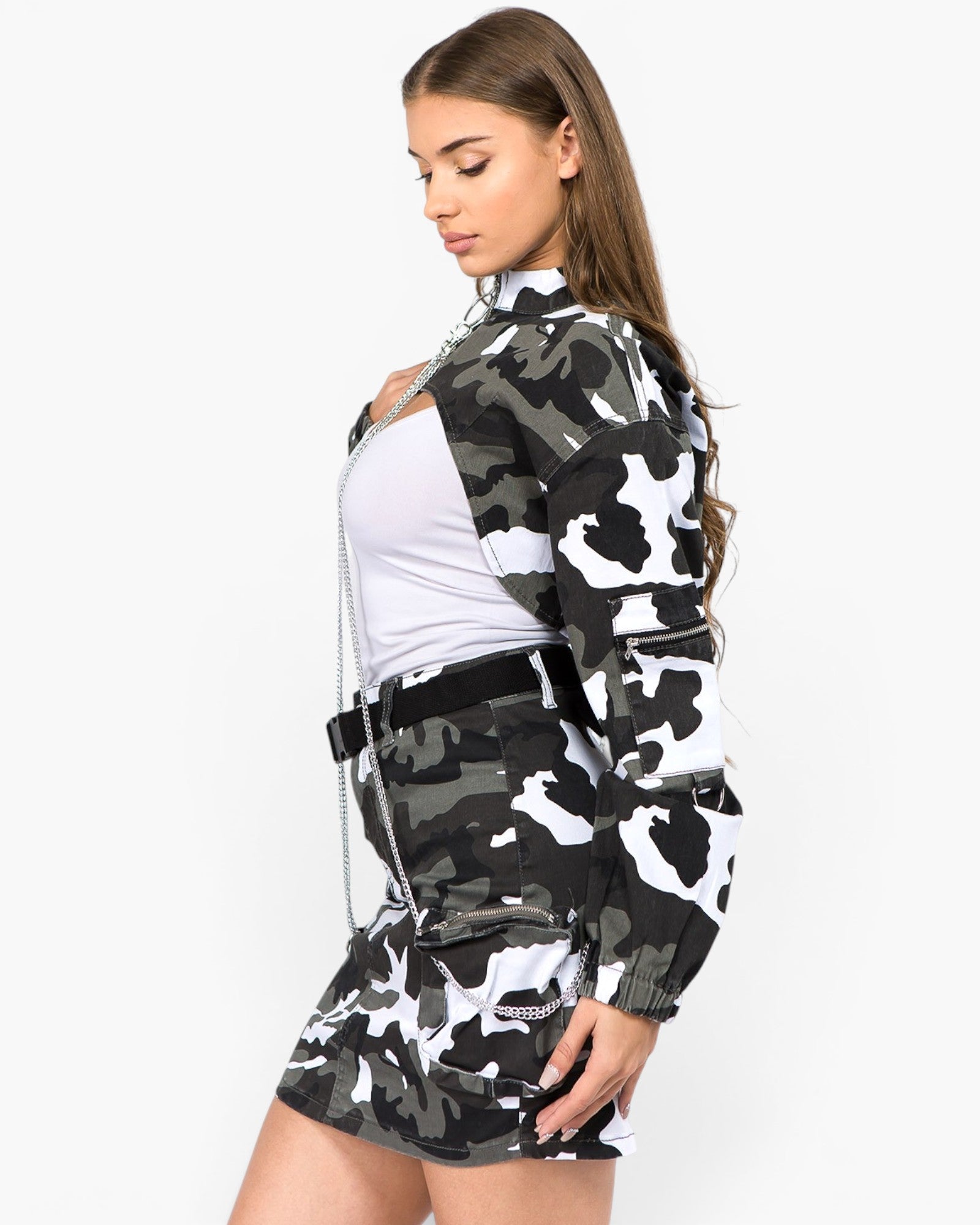 A woman modeling a matching black, gray, and white camouflage jacket and mini skirt set, styled with a white top and a silver chain necklace, against a plain white background.