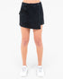 A model from the waist down wearing a dark wash denim mini skirt with a diagonal front slit and a large side cargo pocket, paired with white sneakers on a light gray background.