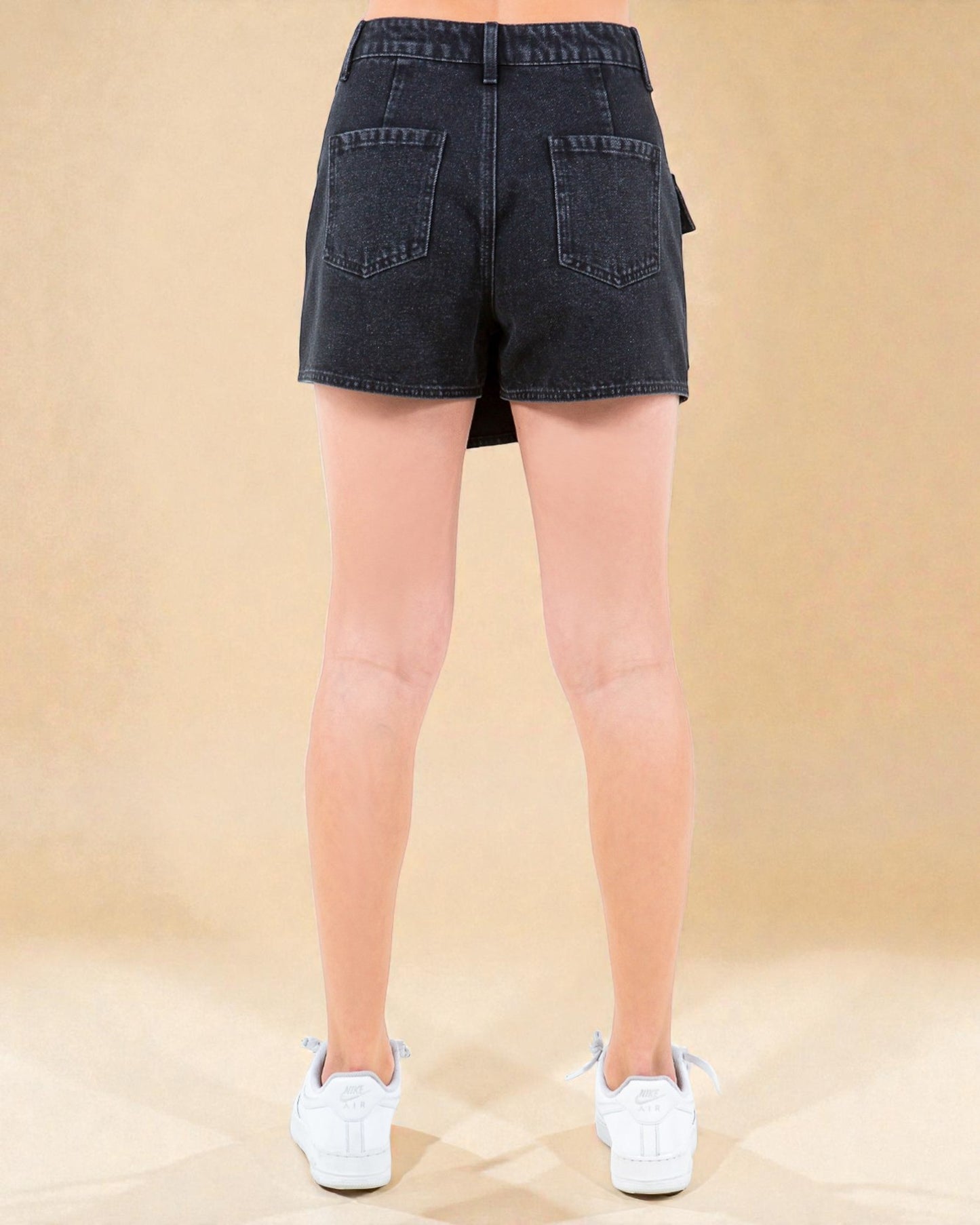 Person wearing black denim shorts on a beige background