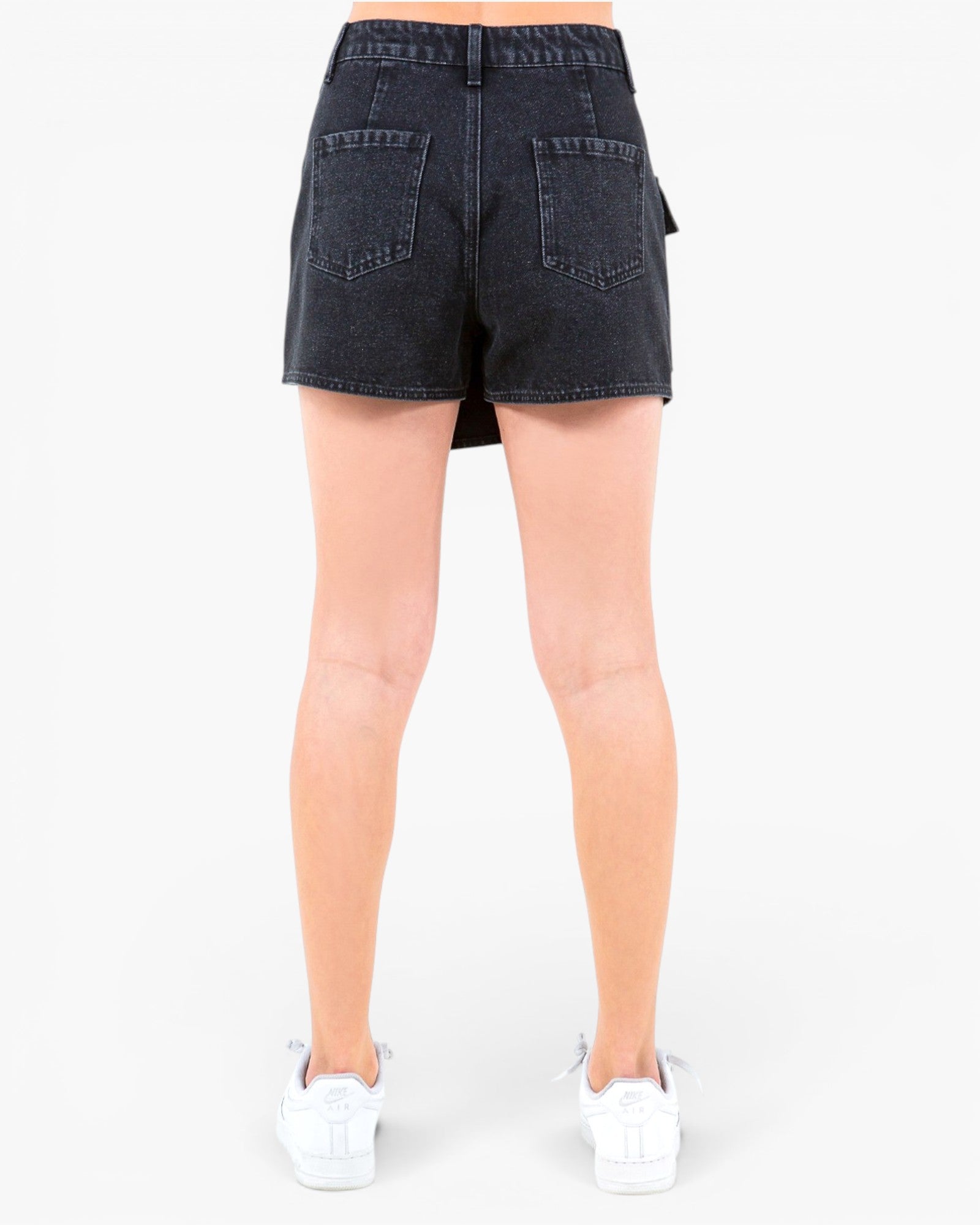 Rear view of a model wearing dark wash denim shorts and white sneakers against a plain white background.