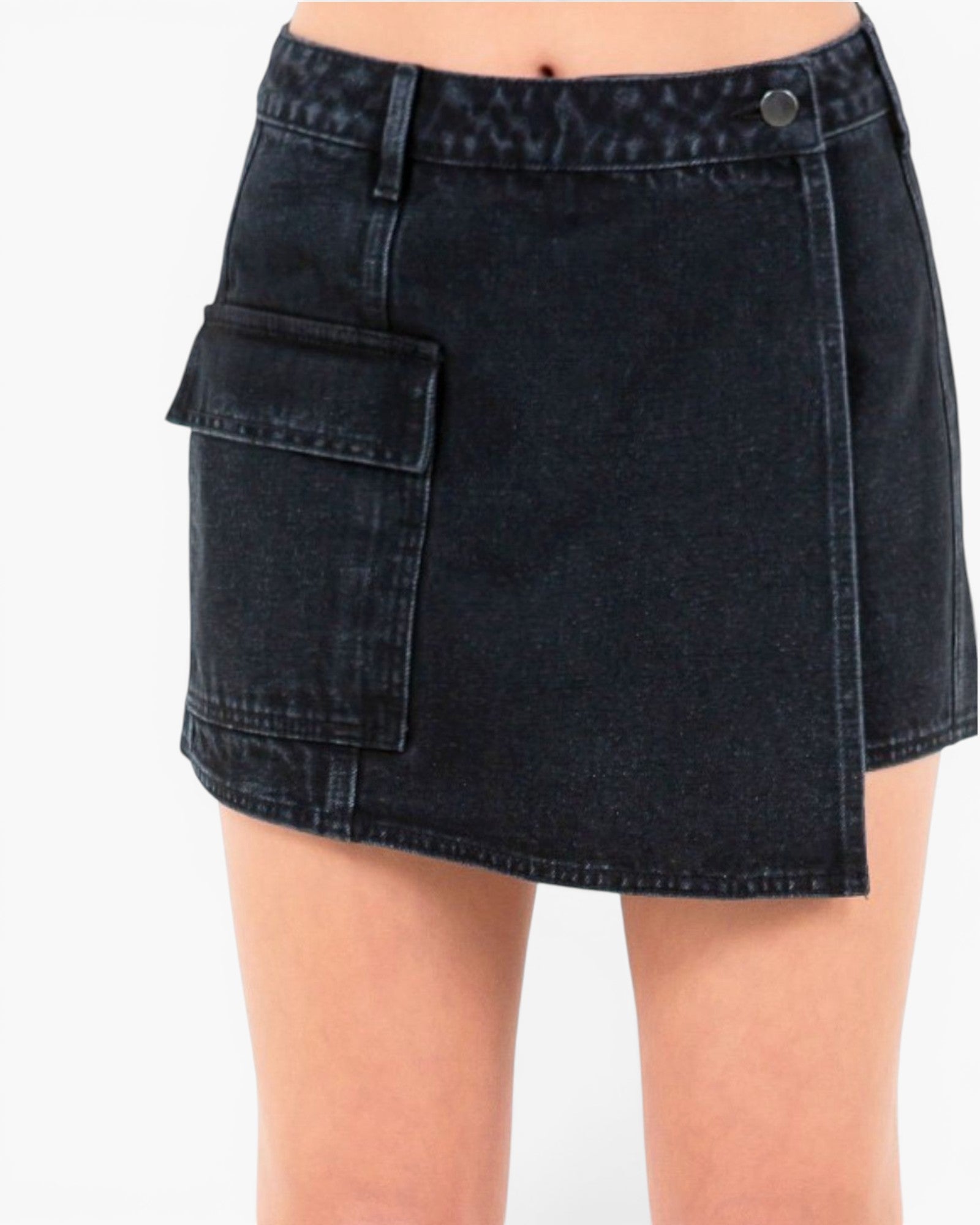 A close-up of a person wearing a dark washed denim mini skirt with an asymmetrical flap pocket, shown against a plain white background.