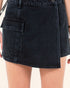Black denim skirt worn by a person on a plain background