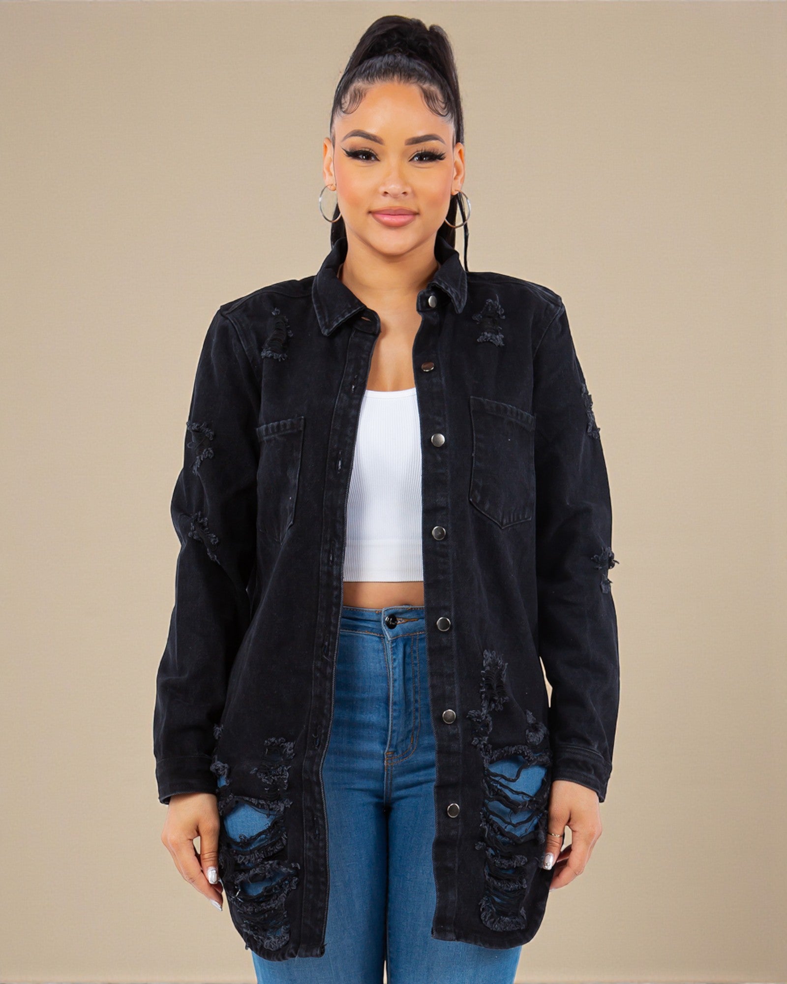 Woman wearing a black distressed denim jacket over a white top and blue jeans on a beige background