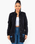 A woman modeling a black distressed denim jacket over a white crop top and blue jeans, photographed against a plain light gray studio background.