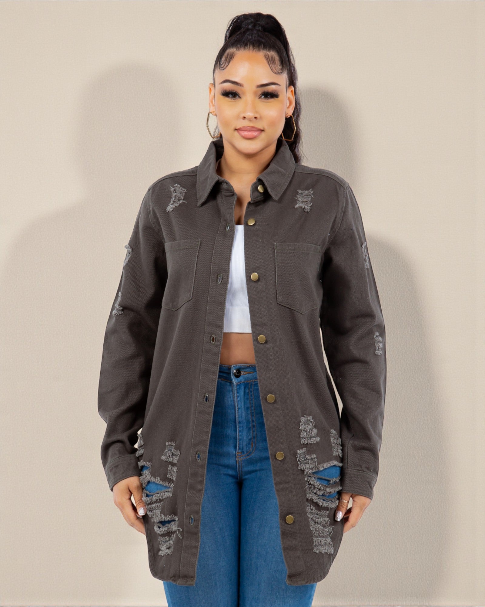 Woman wearing a dark gray distressed jacket and blue jeans against a plain background