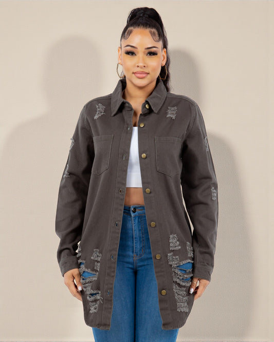 Woman wearing a dark gray distressed jacket and blue jeans against a plain background