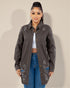 Woman wearing a dark gray distressed jacket and blue jeans against a plain background