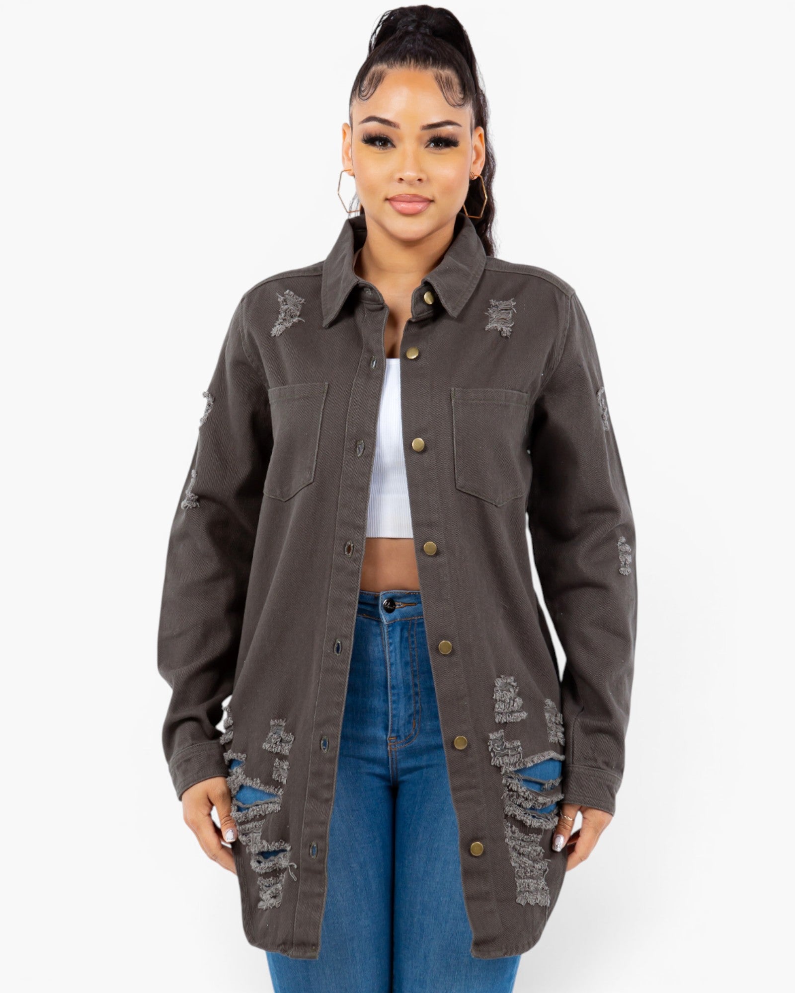 A woman modeling a dark brown distressed button-up shirt jacket with ripped details on the pockets and sleeves, worn over a white crop top and blue jeans against a light gray background.