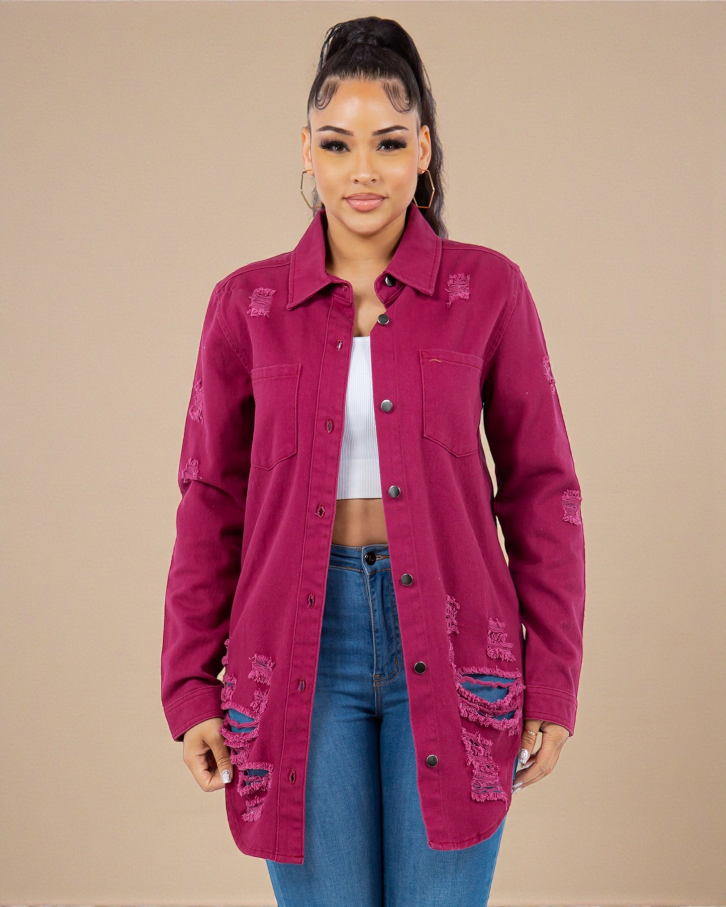 Woman wearing a distressed pink jacket over a white top and blue jeans on a beige background