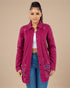 Woman wearing a distressed pink jacket over a white top and blue jeans on a beige background